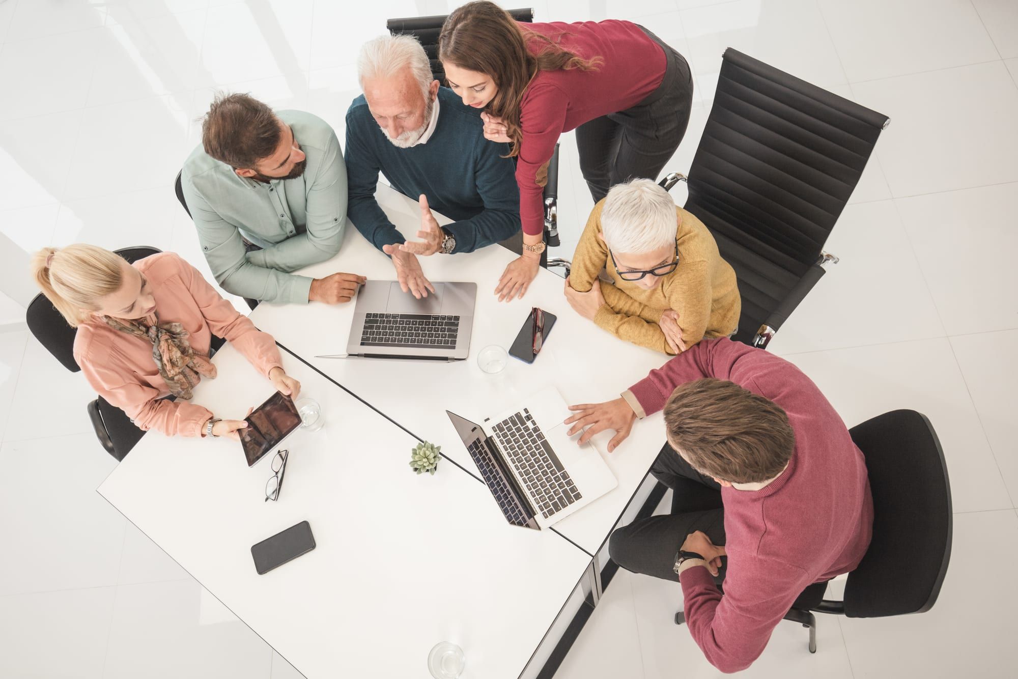 Overhead view of a team collaborating around a white table with laptops