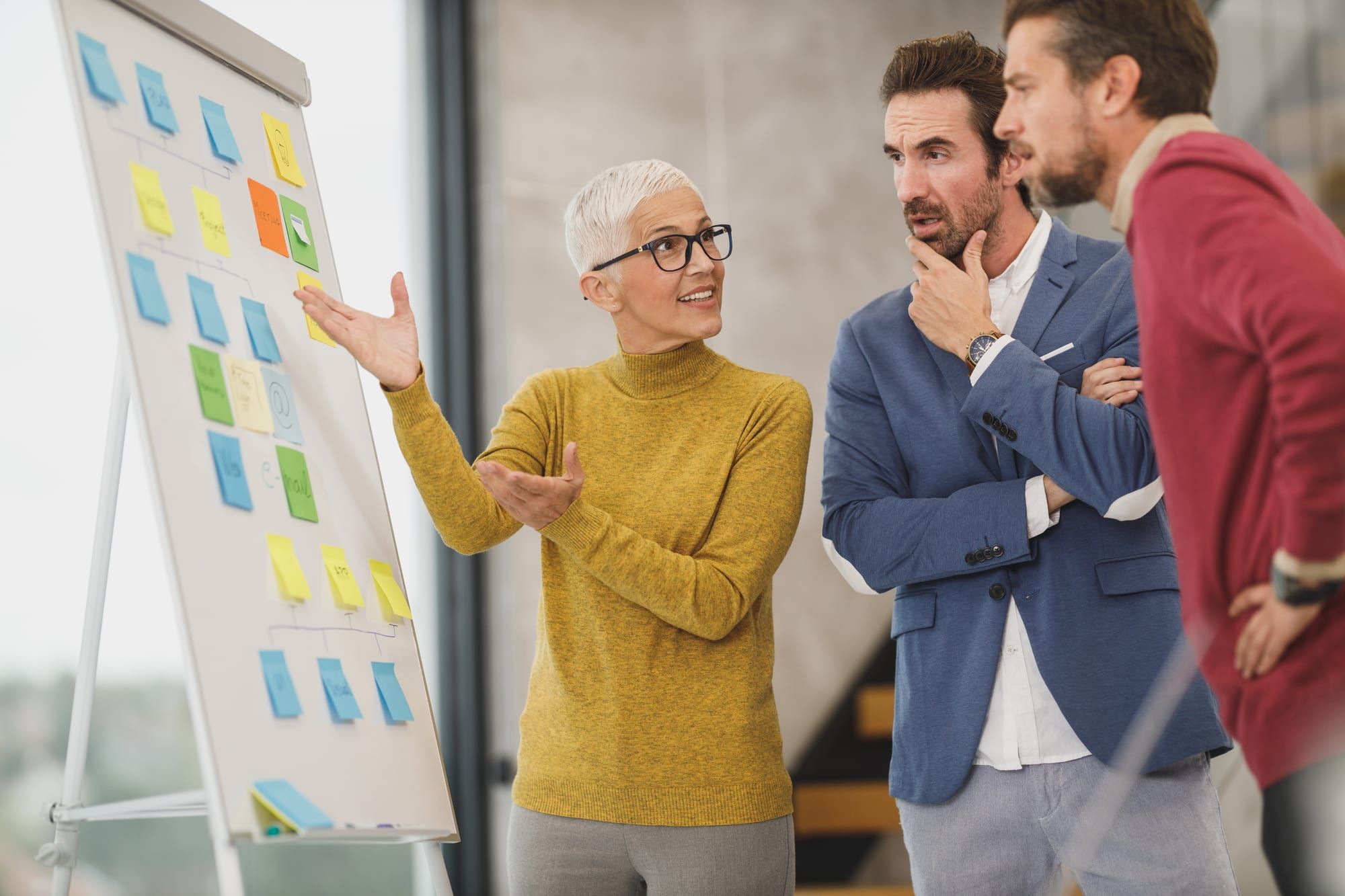 A colleague walking two teammates through a plan on a board of sticky notes