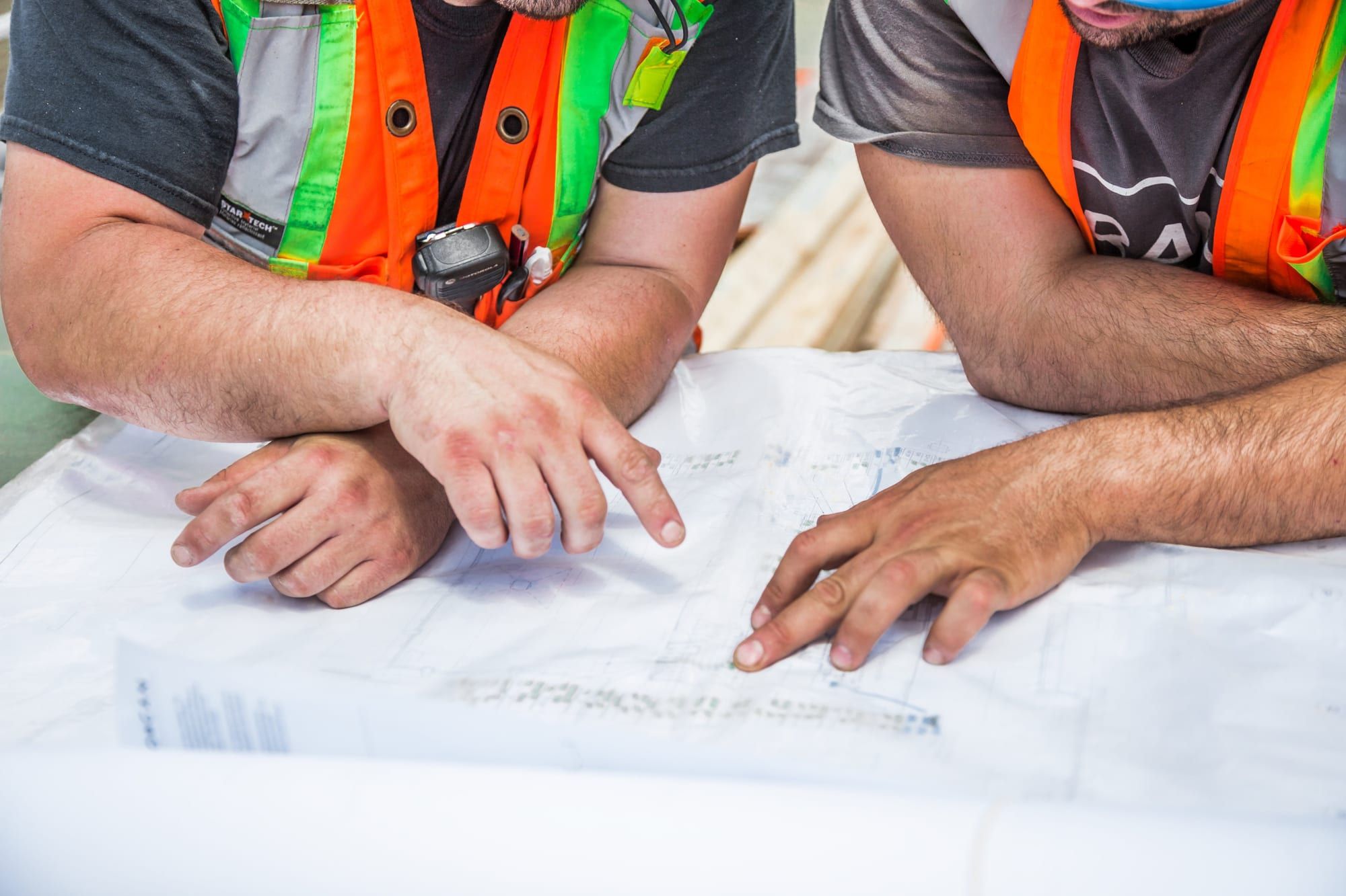 Two workers in safety vests reviewing blueprints on a table